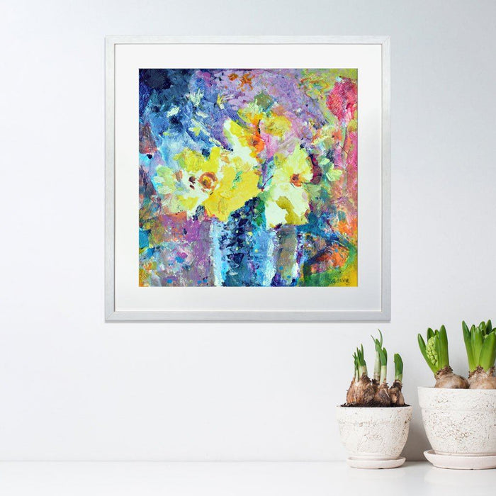 Daffodil Prints from a Daffodil Painting by Judi Glover Art. The Daffodil Wall Art is framed in a light grey frame and is hanging on a wall above a shelf of flowers.
