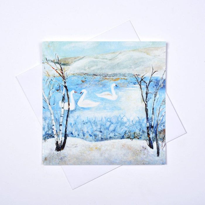 Three white swans swimming on a tranquil blue lake surrounded by snow-covered trees in Judi Glover's A Winter Wonderland set of 6 Christmas cards