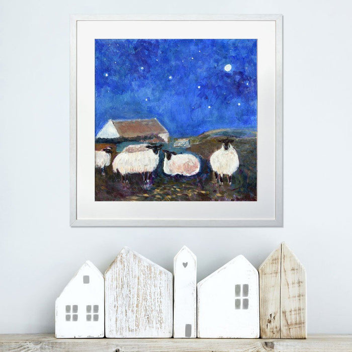 Sheep prints from a painting of sheep under the stars and a dark blue sky. The sheep wall art is framed and hung on a wall above a shelf and available at Judi Glover Art