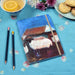Showing the A5 notebook on a table next to pencils, tea and biscuits. The cute notebook has a print of sheep as a cover and is available at Judi Glover Art