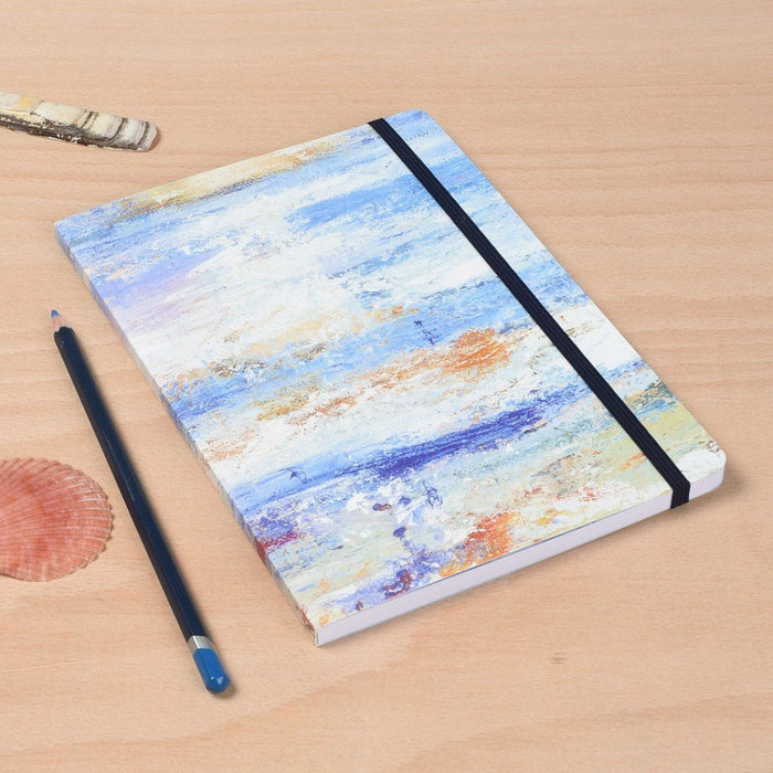 Showing the decorative notebook by Judi Glover Art. The artistic notebook is shown on a table next to a pencil and a shell for scale